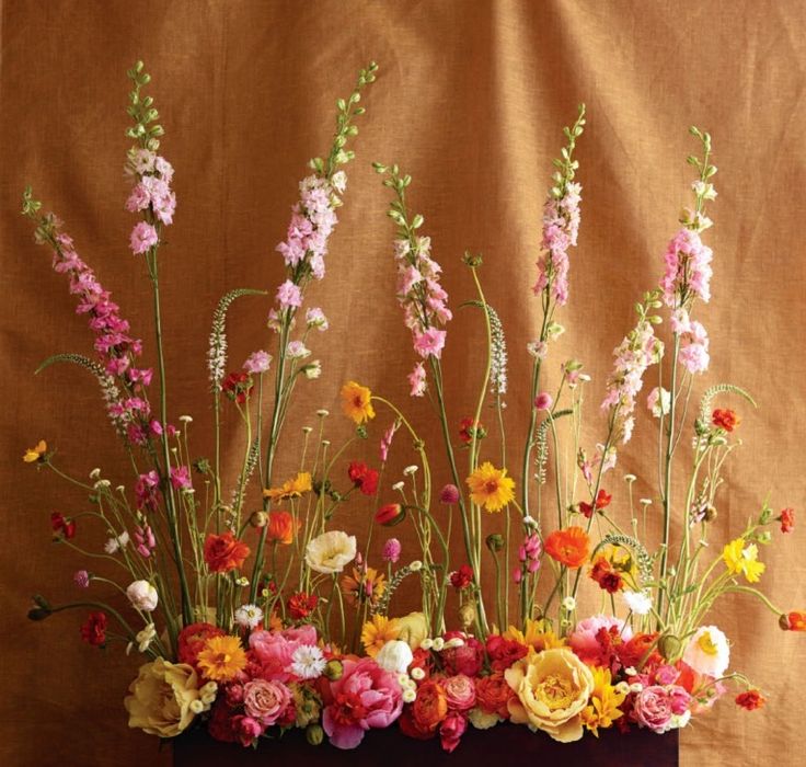 a vase filled with lots of colorful flowers on top of a wooden table next to a brown wall