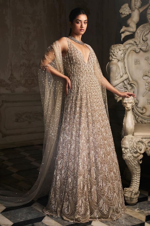 Beige net gown with pearls, sequins and stones embroidered scalloped pattern and tassels.
Components: 1
Pattern: Embroidered
Type Of Work: Pearls, Sequins, Stones
Neckline: Deep V Neck
Sleeve Type: Sleeveless
Fabric: Net
Color: Beige
Other Details: 
Closure: Back zip
Note: Dupatta worn by the model is not for sale.
Occasion: Cocktail,Reception - Aza Fashions Pink Sequin Lehenga, V Neck Gown, Pearl Tassels, Seema Gujral, Net Gowns, Gown For Women, Simple Pakistani Dresses, Ladies Gown, Tulle Gown