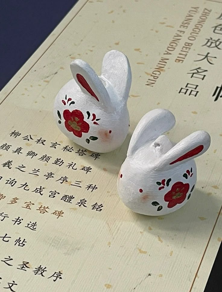 two white ceramic rabbits sitting on top of a piece of paper with chinese writing in the background