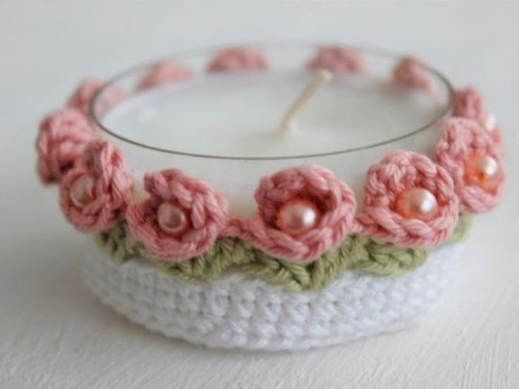 a crocheted candle holder with a pink flower on the front and green trim around it