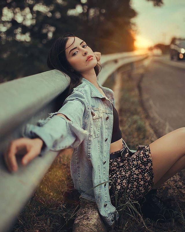 a woman sitting on the side of a road next to a metal rail with her hand under her chin