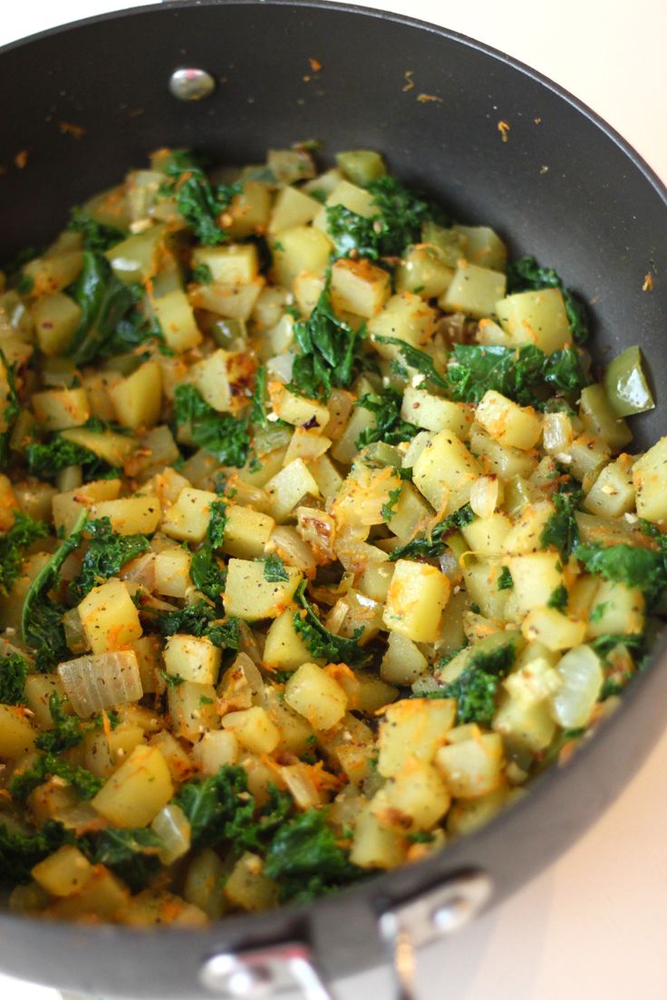 a pan filled with potatoes and spinach on top of a stove burner next to a spatula