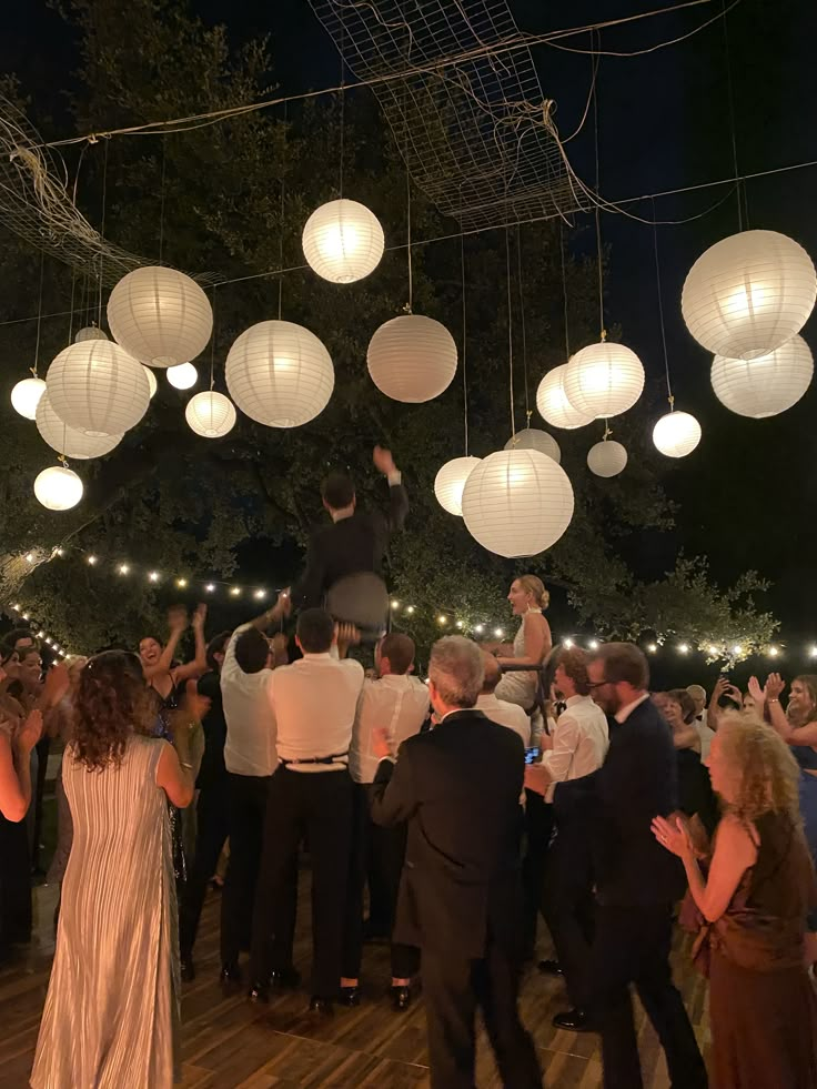 a group of people standing on top of a wooden floor covered in paper lantern lights