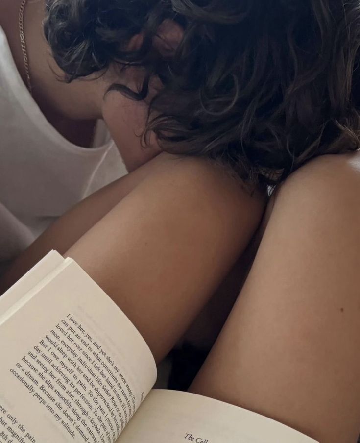 a woman laying down reading a book with her arm wrapped around her neck and head