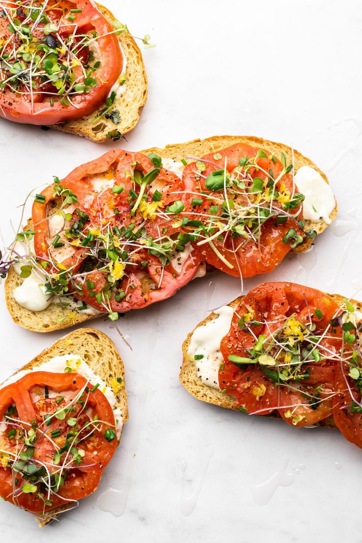 four slices of bread with tomatoes and herbs on top, sitting on a white surface