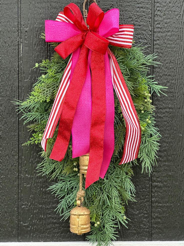 a christmas wreath hanging on the side of a door with a red bow and bell