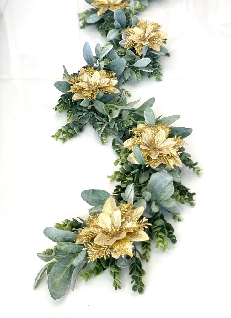 three gold flowers and green leaves on a white table top with text overlay that reads, how to make faux floral garlands