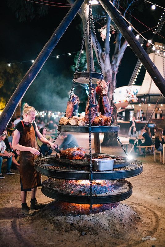 a woman cooking food on top of a grill in the middle of an outdoor area