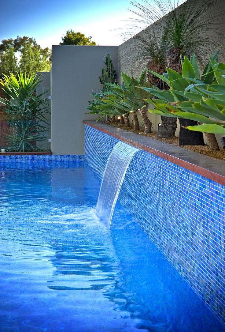 a blue swimming pool with water running down it's sides and plants growing on the side