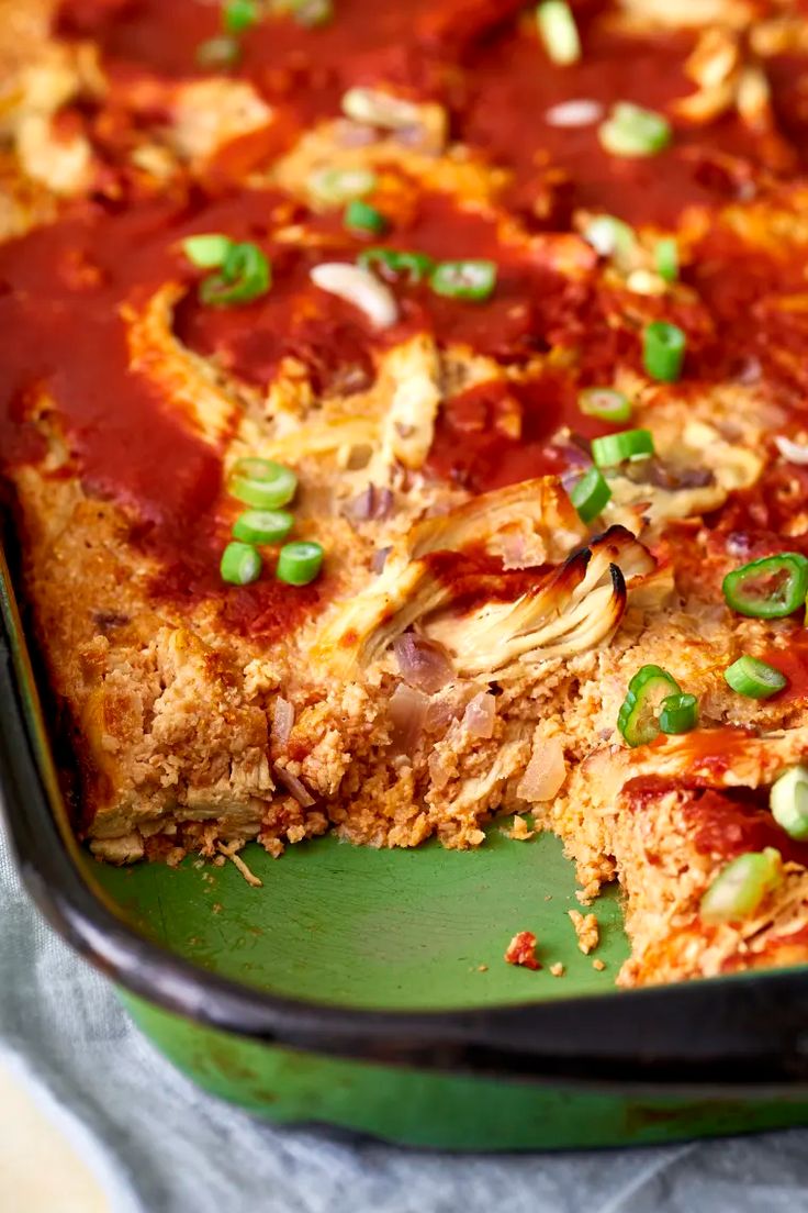 a green casserole dish filled with meat and veggies, topped with sauce