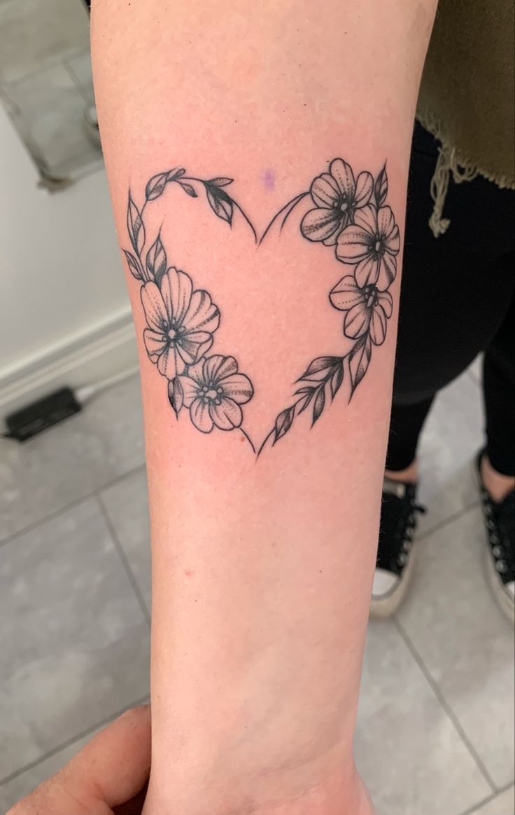 a heart shaped tattoo with flowers on the arm