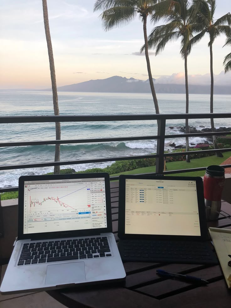 two laptops are sitting on a table near the ocean