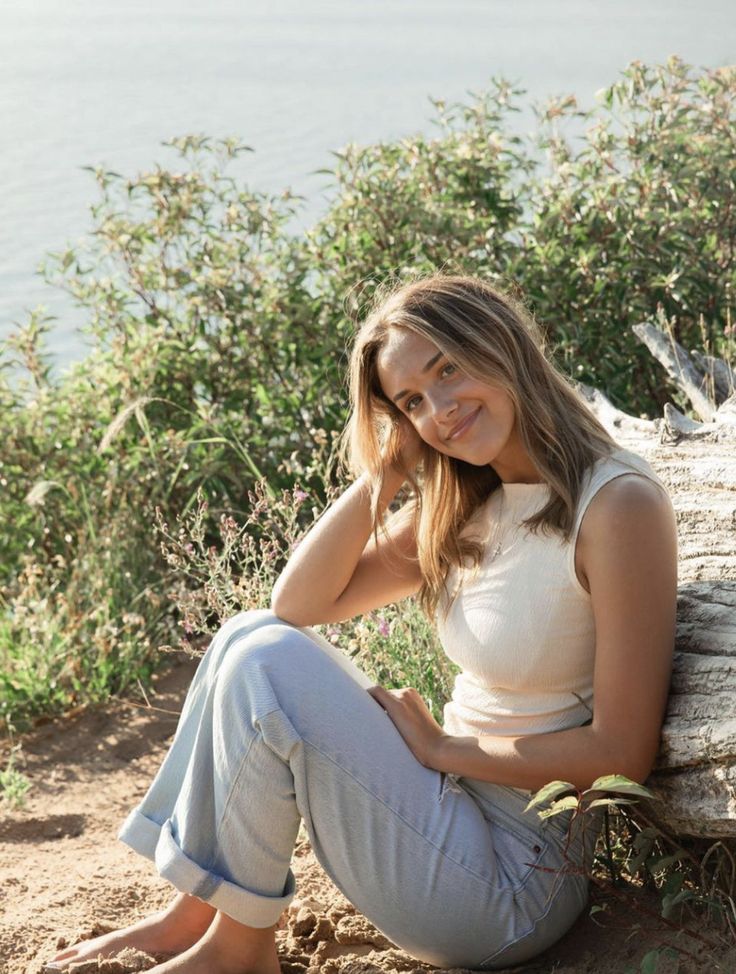 a beautiful young woman sitting on top of a log