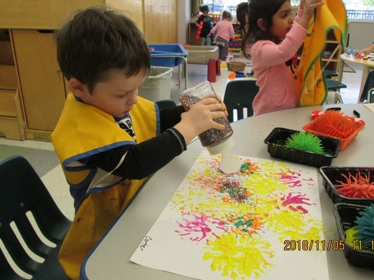 a young boy sitting at a table making art with colored paper and plastic straws