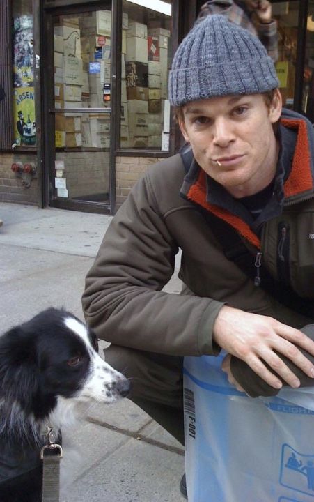 a man sitting next to a black and white dog on the sidewalk with a trash can