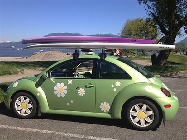 a green car with flowers painted on it and a surfboard strapped to the roof