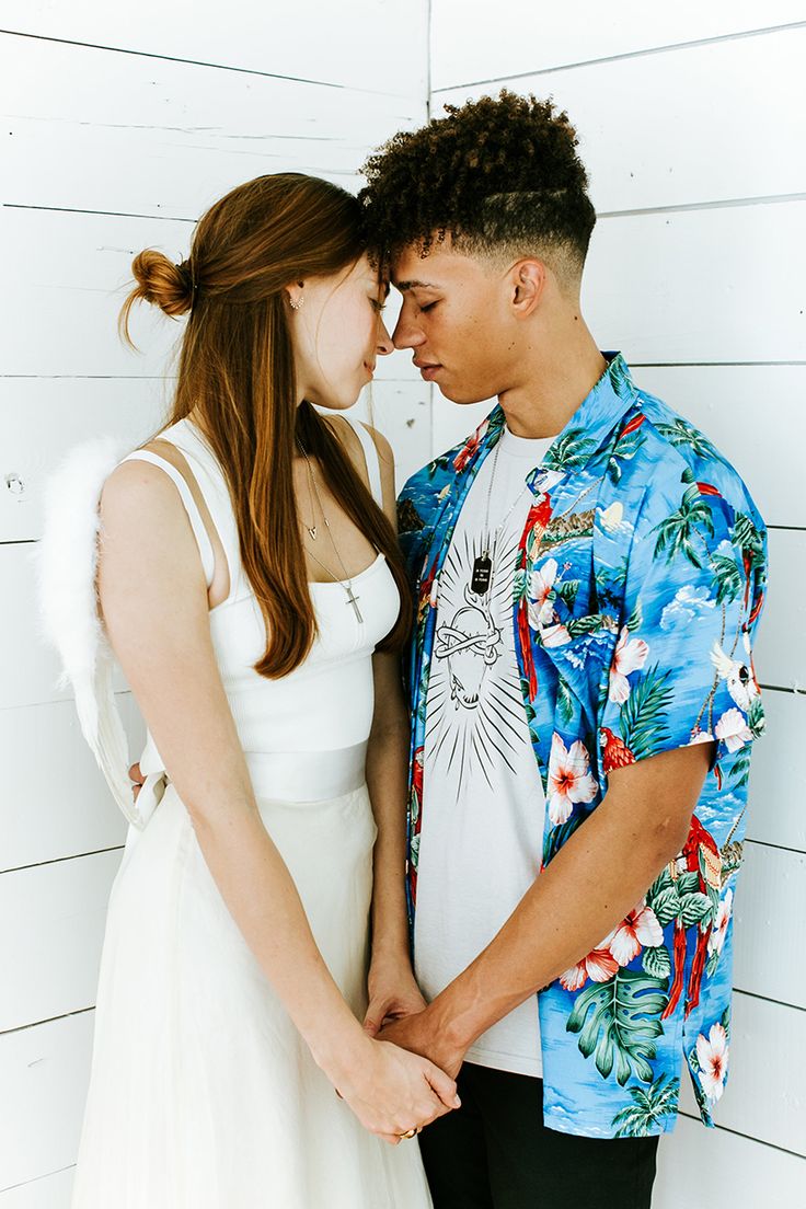 a young man and woman standing next to each other in front of a white wall