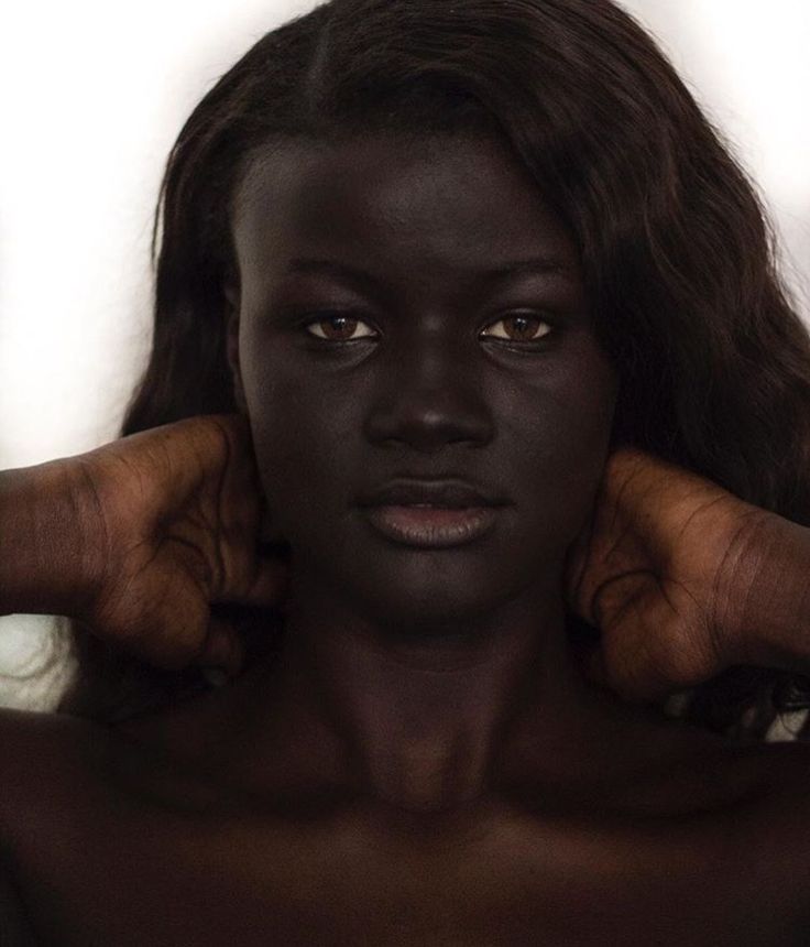 a woman with dark skin and hands on her head is posing for the camera in front of a white background