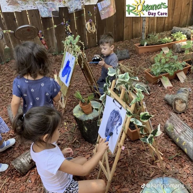 three children are painting pictures in the garden with easels and potted plants on the ground