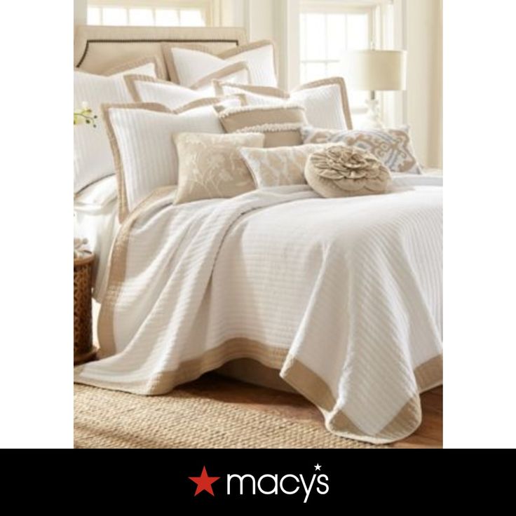 a bed with white sheets and pillows in a room next to a window that says macy's