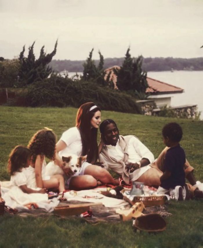 a group of people sitting on top of a lush green field next to a lake