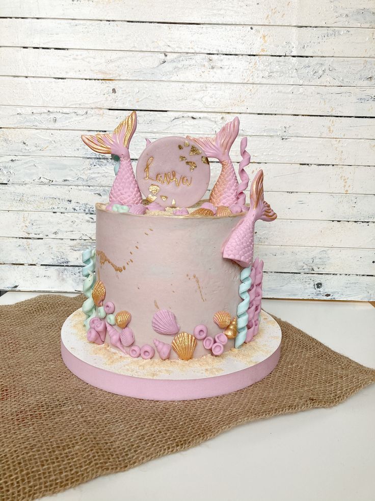 there is a pink cake with mermaid decorations on it