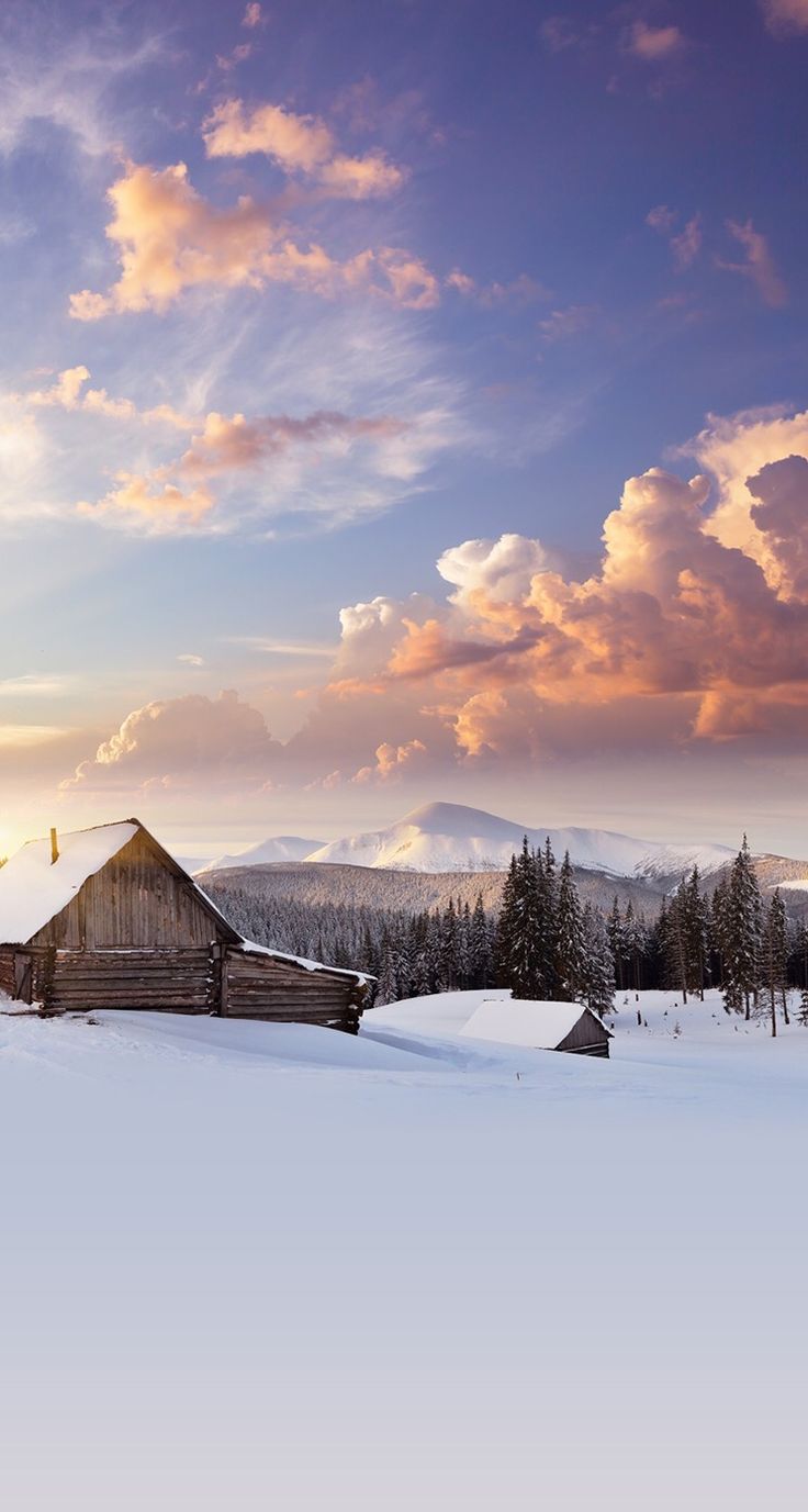 a barn in the middle of a snow covered field with mountains in the back ground