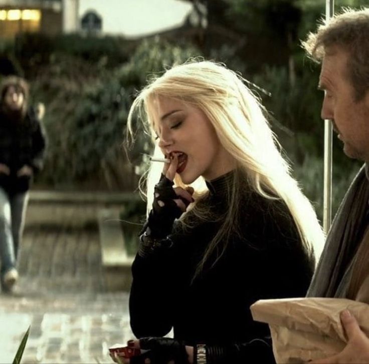 a man and woman sitting at a table with food in front of them, talking on the phone