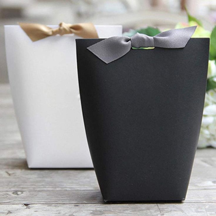 two black and white bags with bows on them sitting on a table next to flowers