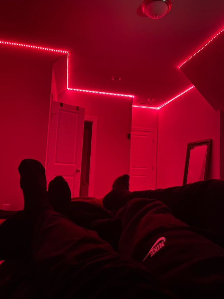 a person laying down in a dark room with red lights on the ceiling and their feet up