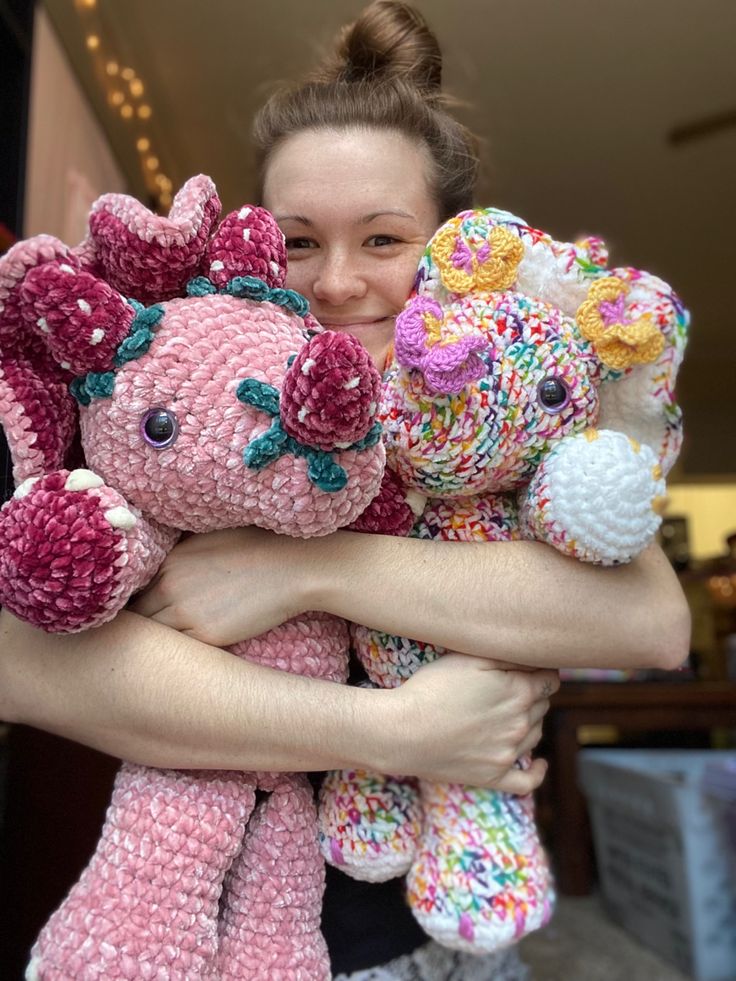 a woman is holding two crocheted stuffed animals in her arms and smiling at the camera