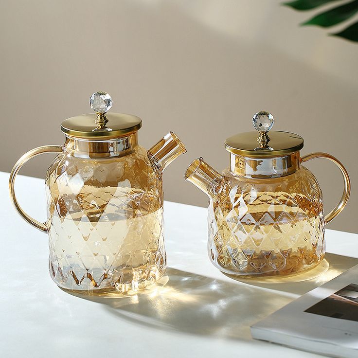 two glass teapots sitting on top of a table next to a cell phone