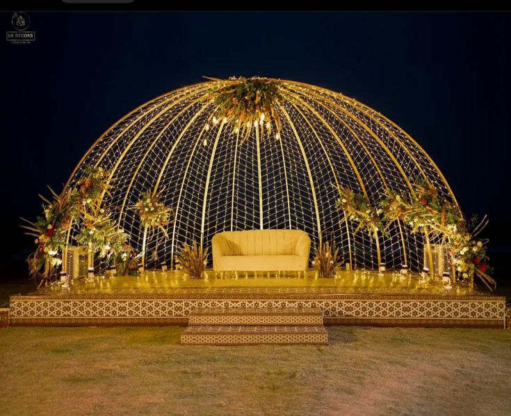 a couch sitting under a lit up dome in the middle of a field at night