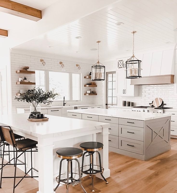 a large kitchen with white cabinets and wooden flooring, along with two bar stools