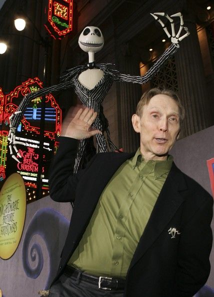 a man in a green shirt and black blazer is holding up a skeleton statue