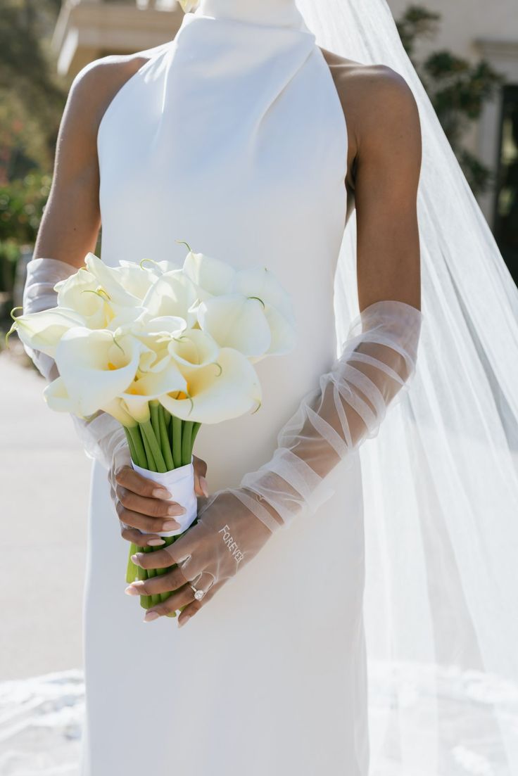 a woman in a white wedding dress holding a bouquet of flowers and wearing a veil