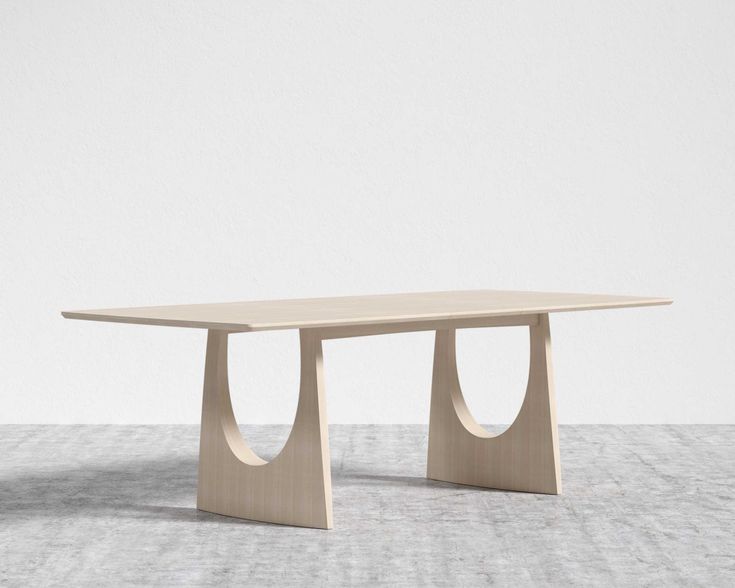 a wooden table with two curves on the top and one curved at the base, in front of a white wall