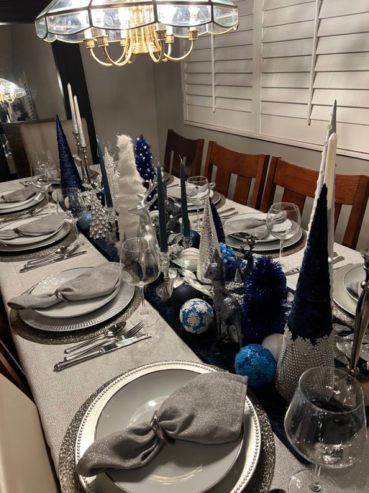 a dining room table set for christmas with blue and silver decorations on the place settings