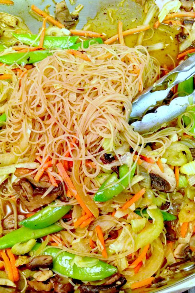 noodles and vegetables are being cooked in a wok with tongs on the side