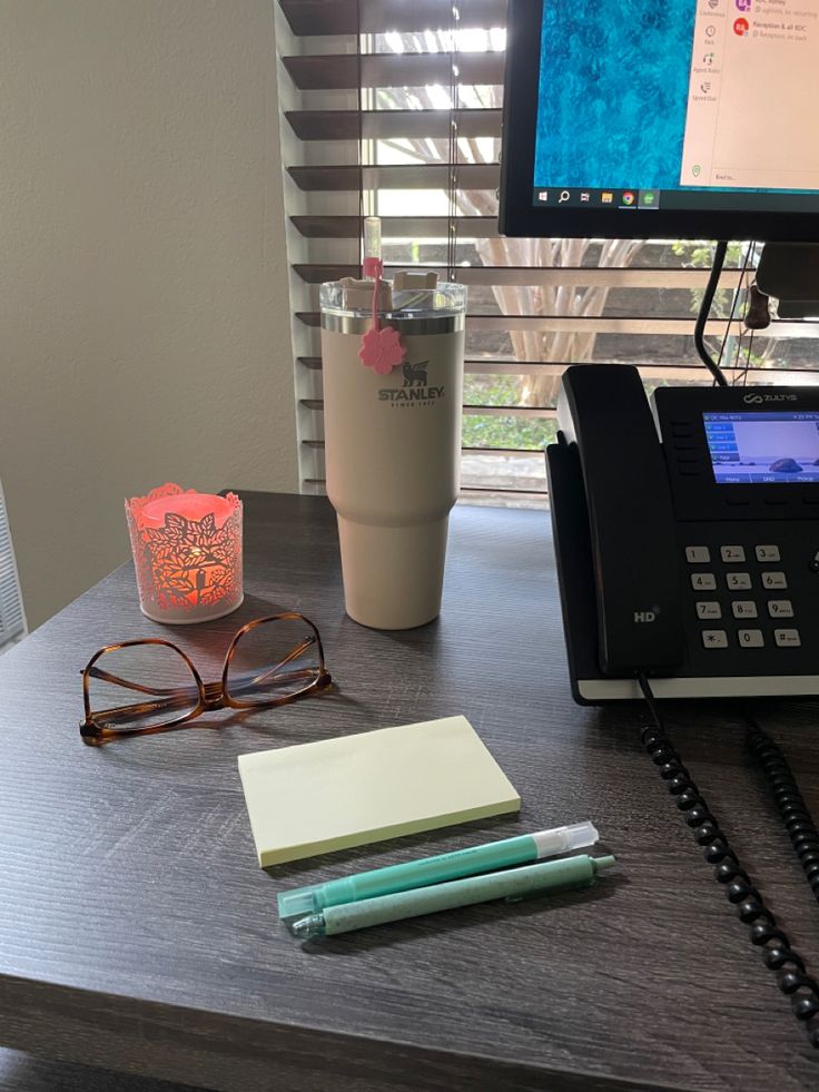 a desk with a phone, pen and glasses on it next to a computer monitor