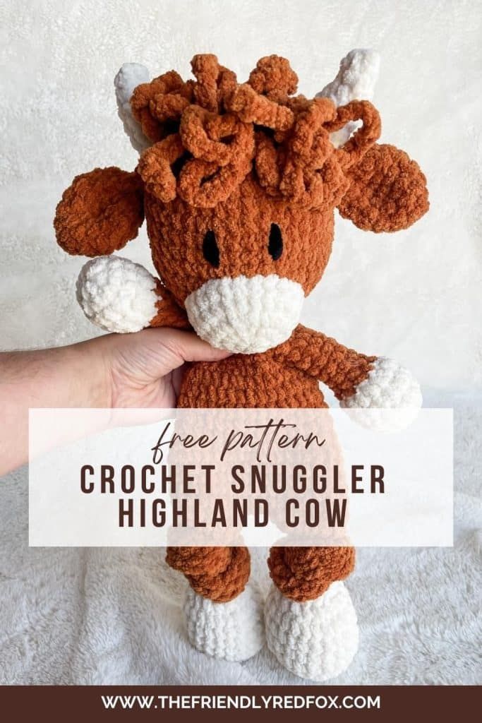 a hand holding a small crochet snuggler in the shape of a cow