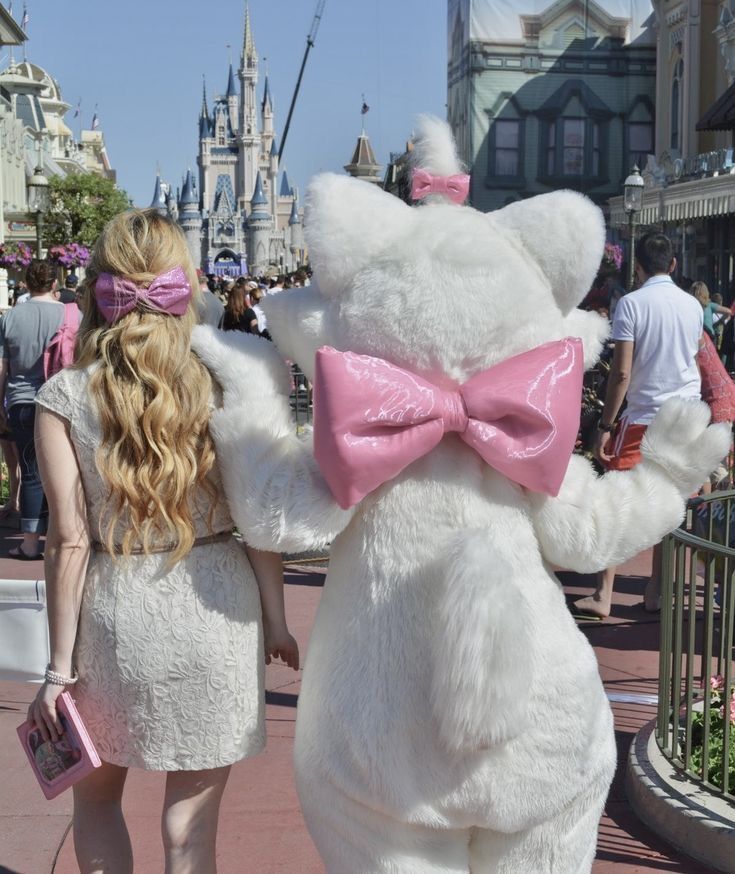 a woman in a white dress and pink bow tie standing next to a large teddy bear