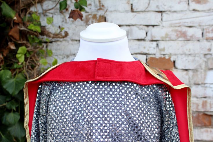 a white mannequin with a red cape on it's head is standing in front of a brick wall