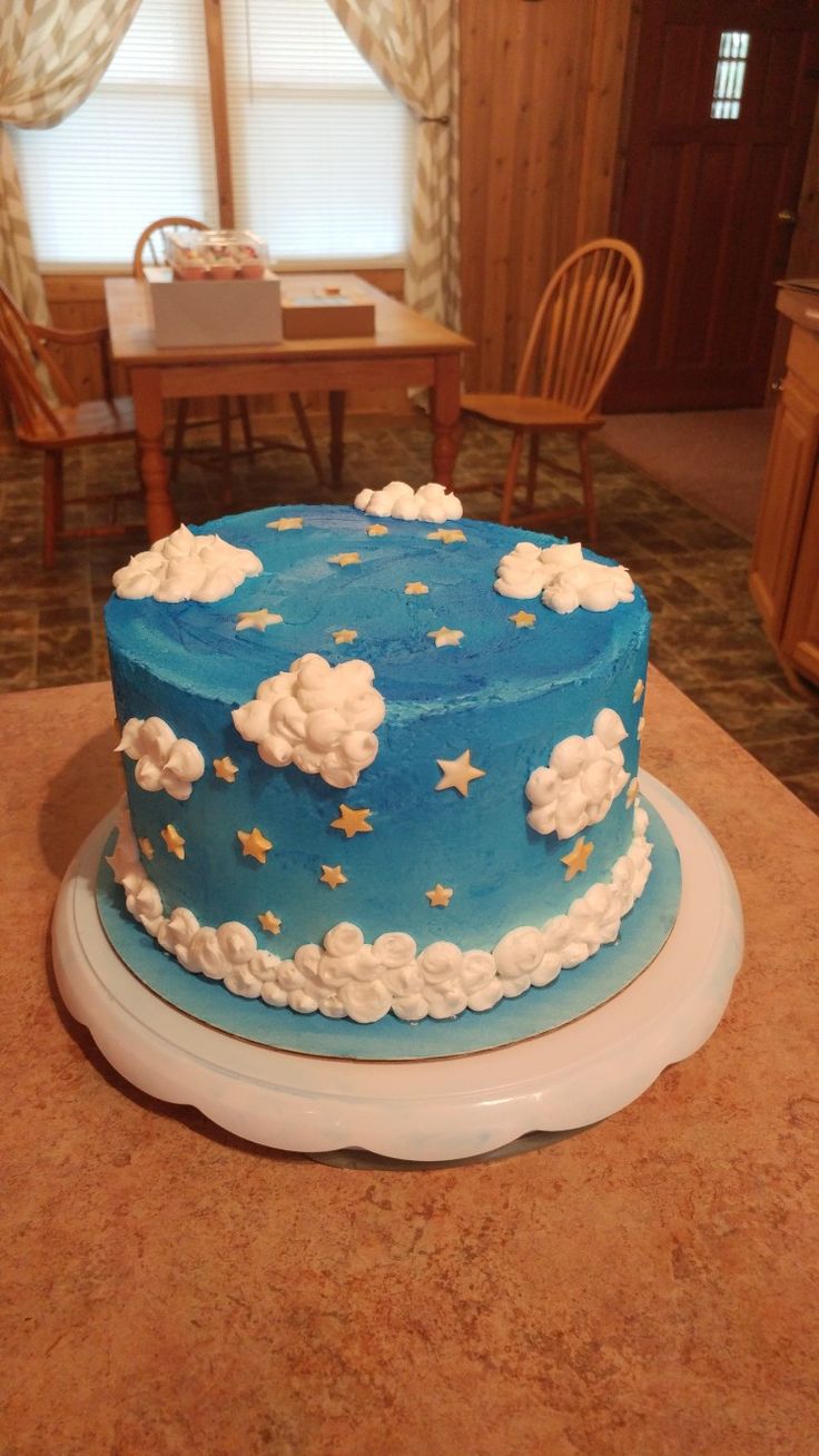 a blue cake with clouds and stars on it sitting on a table in front of a window