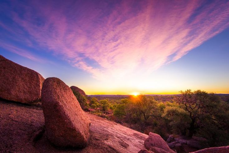 the sun is setting over some rocks and trees