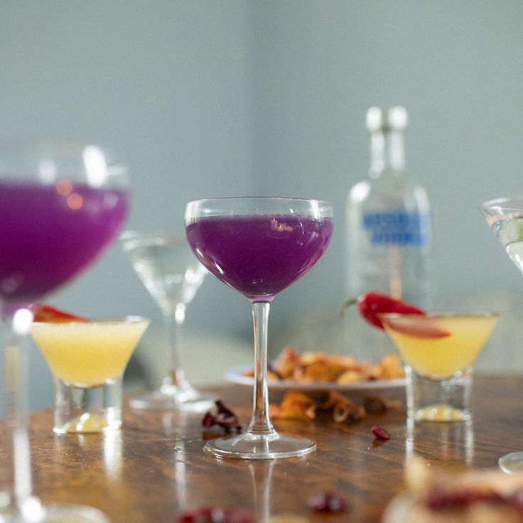 there are many different drinks in the glasses on the table, one is purple and one is yellow