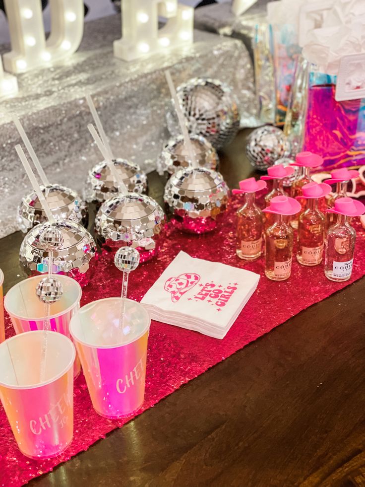 the table is set up with pink and silver decorations, glasses, and napkins