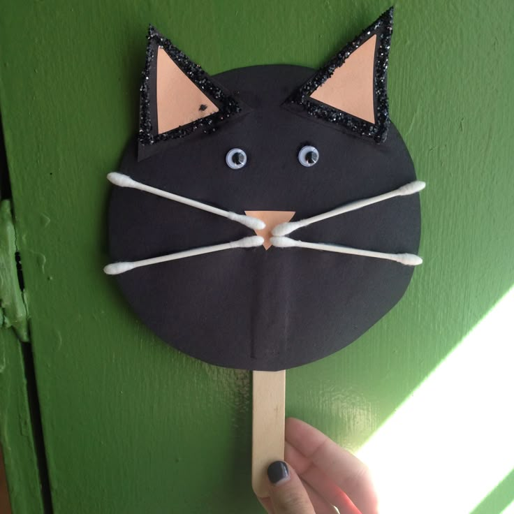 a hand holding up a black cat mask on a green door with white string attached to it