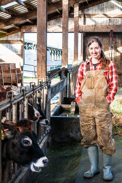 a woman in overalls standing next to cows