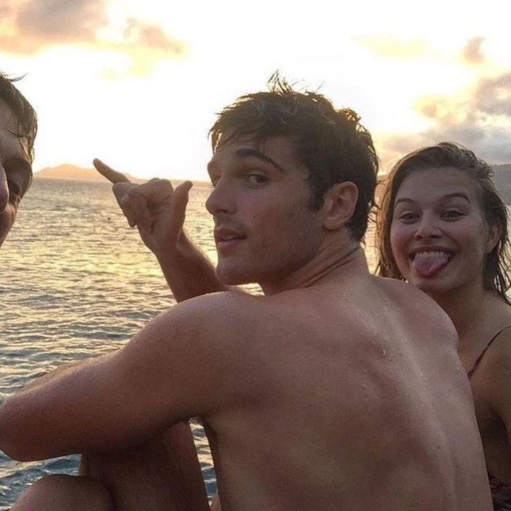 three people sitting on the edge of a boat at sunset, one man is holding a toothbrush in his other hand